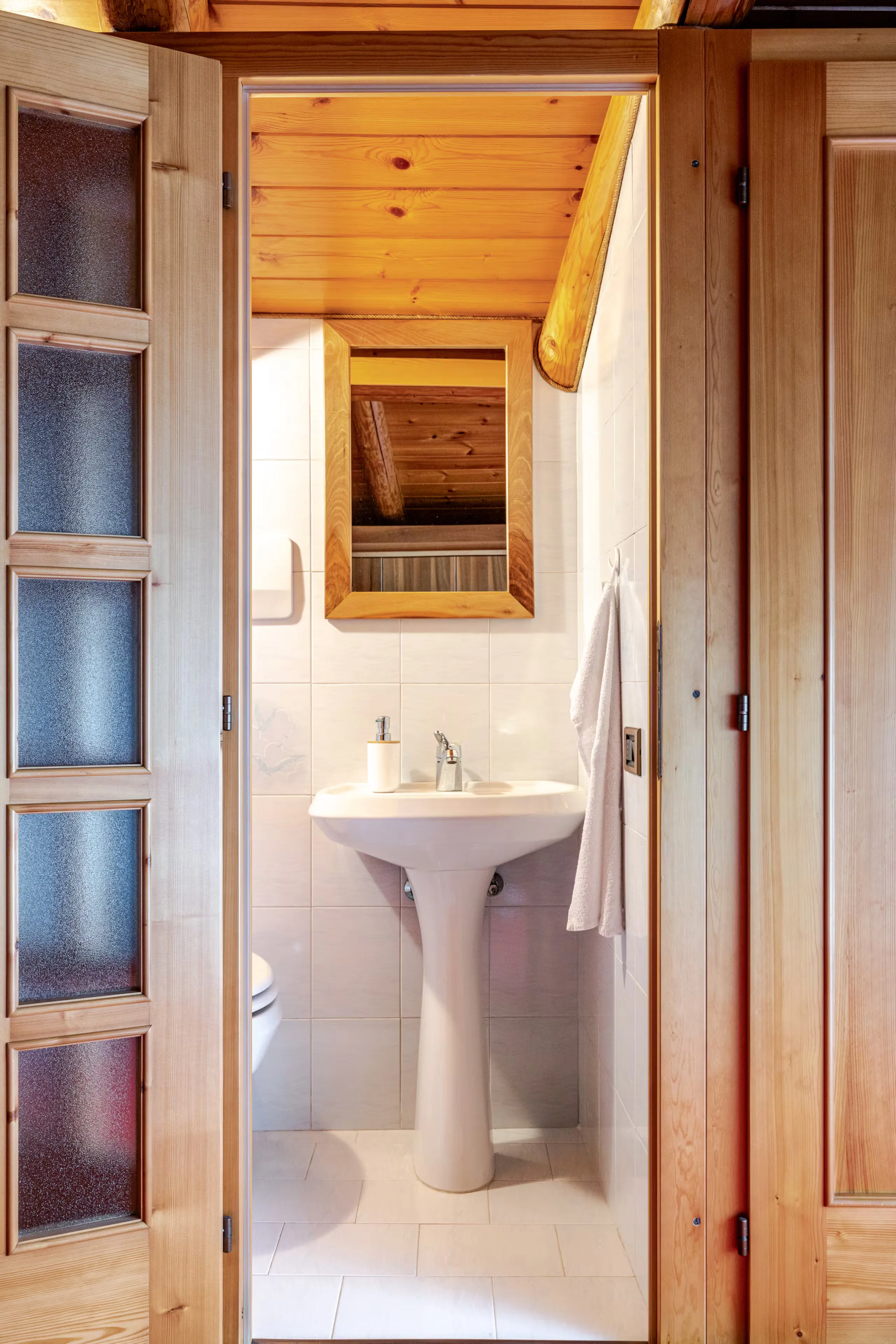 Ingresso del bagnetto in camera, con lavabo bianco e specchio che riflette le travi