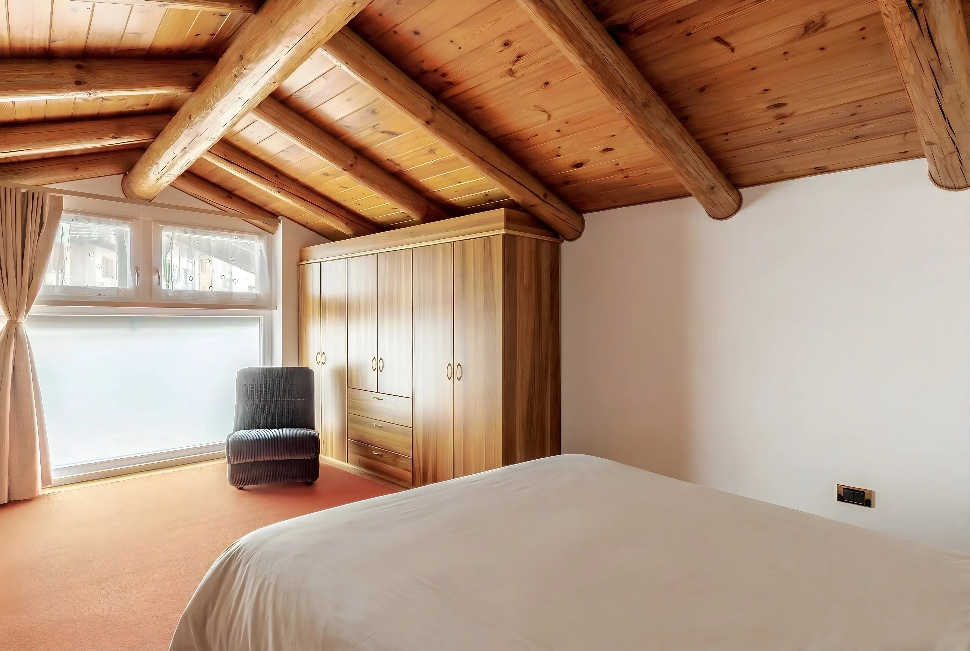 Camera da letto con armadio in legno, poltrona e finestra con tende chiare