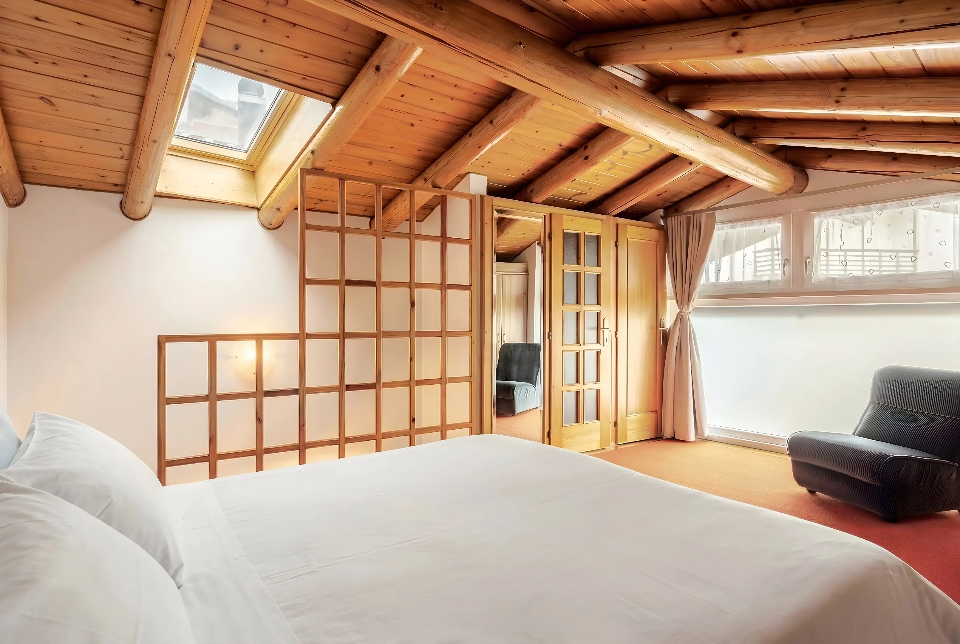 Camera matrimoniale con lucernario, finestra e poltrona scura sotto il soffitto in legno