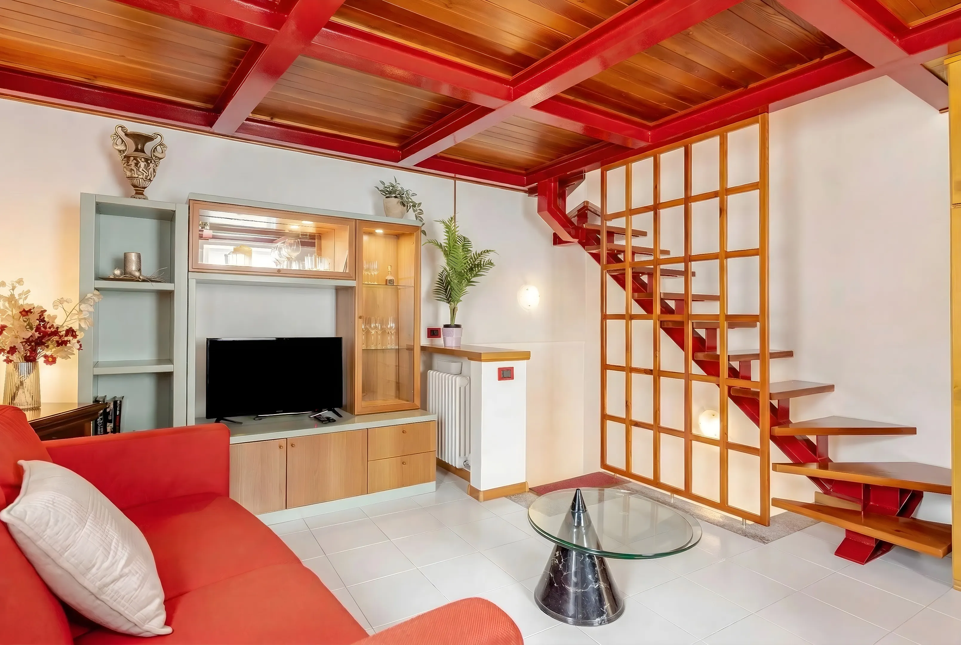 Il soggiorno di Casa Al Vicolo, con divano rosso, travi a vista e scala in legno